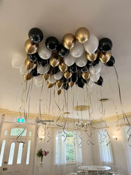 Decorative arrangement of black, gold, and white balloons in a room with large windows.