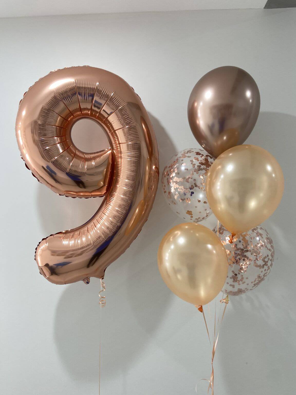 Rose gold number 9 balloon and other balloons on a white background