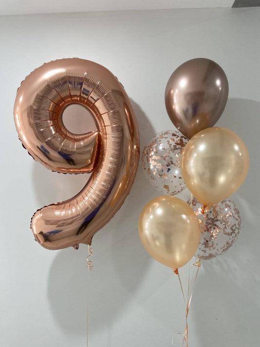 Rose gold number 9 balloon and other balloons on a white background