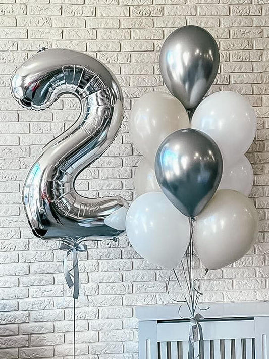 Silver number '2' balloon and white balloons against a light brick wall.
