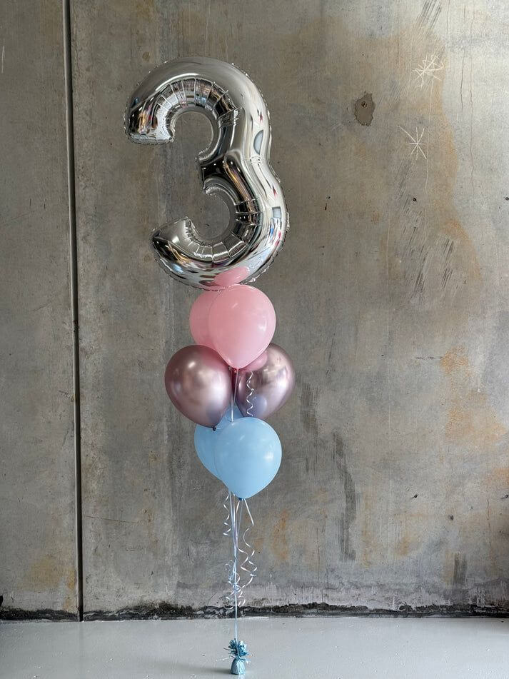 Silver number '3' balloon with pink, blue, and purple balloons against a textured wall.