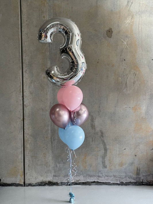 Silver number '3' balloon with pink, blue, and purple balloons against a textured wall.